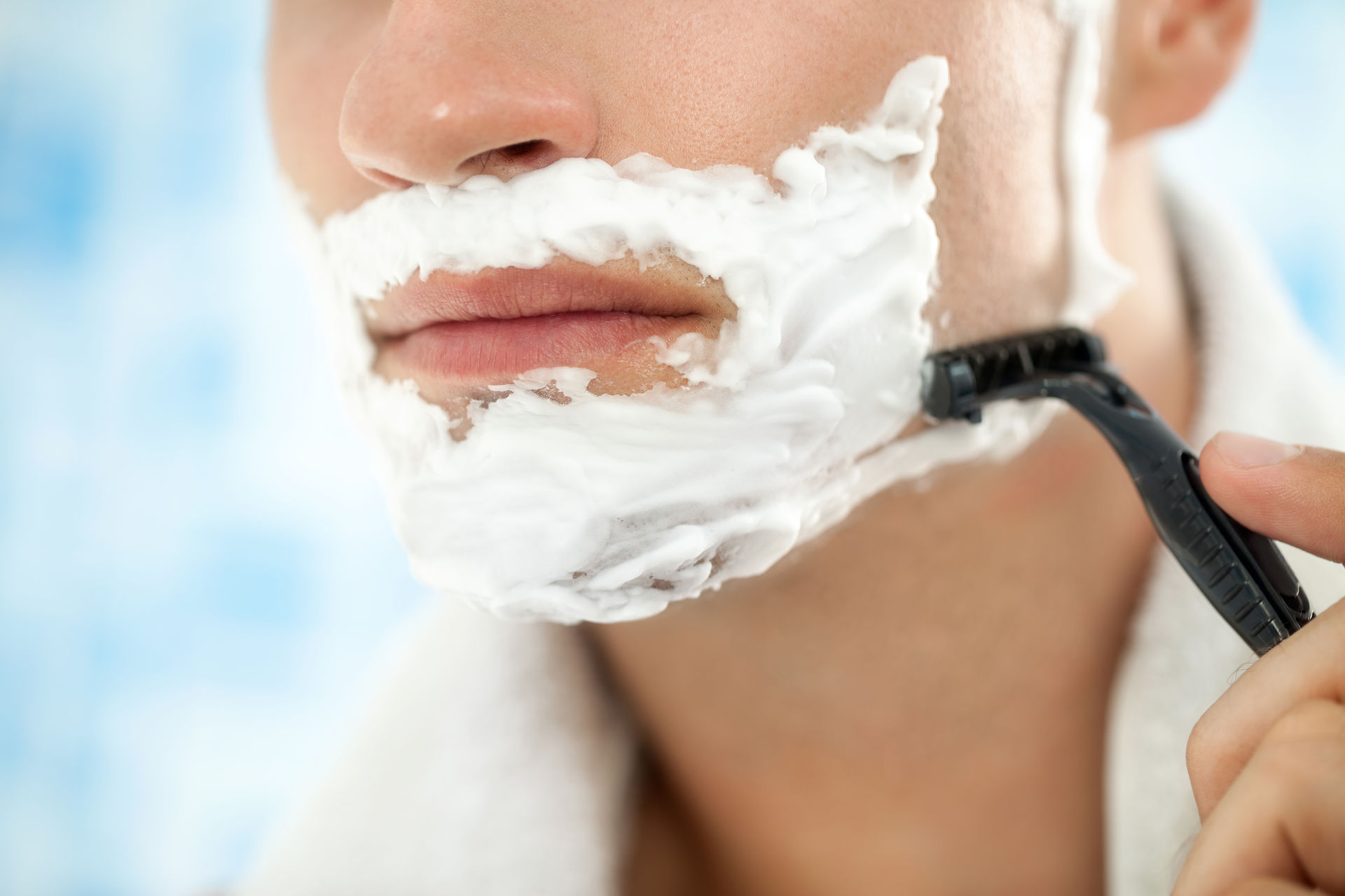 Male shaving facial hair with razor and shaving cream on face